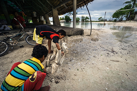 Children building a sea wall to protect a maneaba against rising sea level in South Tarawa.  The heart of any Kiribati community is its maneaba or meeting house. A traditional maneaba has an imposing structure, with slabs of coral supporting a huge roof formed from coconut wood, held together with coconut string and thatched with pandanus leaves. The whole community is involved in its construction, and every aspect of the maneaba has a symbolic as well as a practical function.