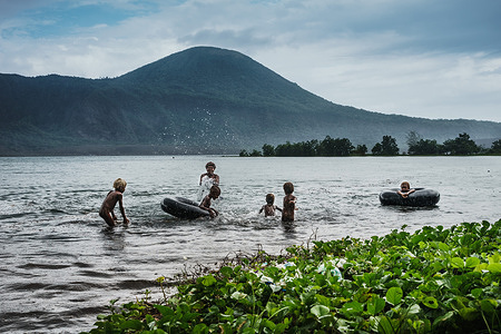 Children playing in water.In the background, Rabaul volcano (Tavurvur). Rabaul Volcano is one of the most active and most dangerous volcanoes in Papua New Guinea. It exploded violently in 1994 and devastated the lively city of Rabaul.